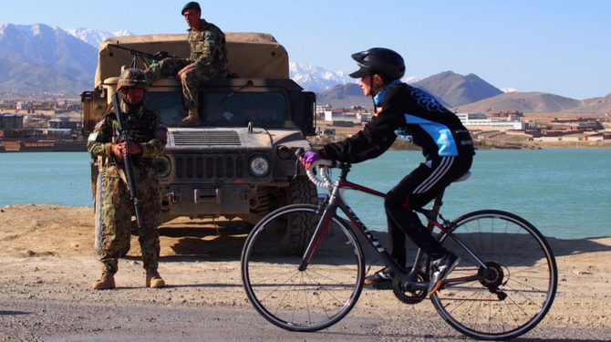 A cyclist riding past troops in Afghanistan