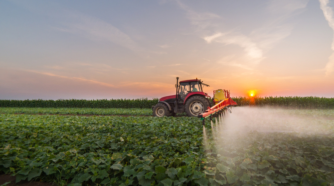 Tractor spraying pesticides over a field of crops