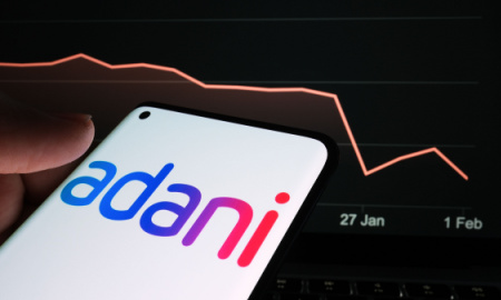 Adani Group logo seen on the smartphone screen and company stock price drop graph seen on the blurred background. Real stock chart for a month timeframe. Stafford, United Kingdom, February 2, 2023