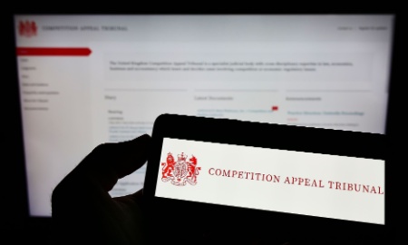 Person holding cellphone with logo of British body Competition Appeal Tribunal (CAT) on screen in front of webpage. Focus on phone display. Unmodified photo.